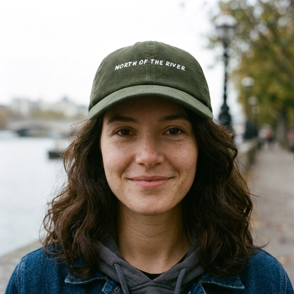 Woman wearing the North of the River corduroy cap in Dark Olive on the north bank of the Thames, Islington, North London