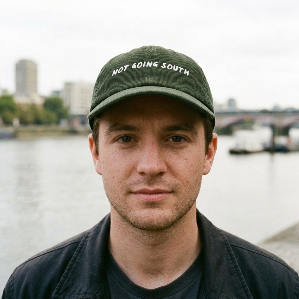 Man wearing the Not Going South corduroy cap in Dark Olive on the north bank of the Thames, Islington, North London